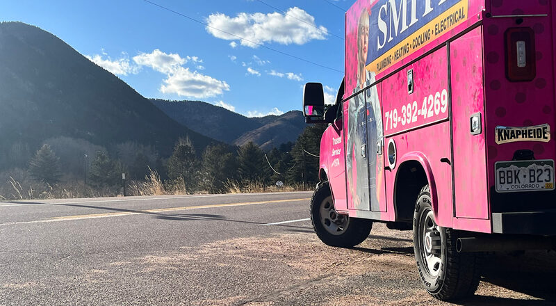 A Smith pink utility truck parked on a Colorado mountain road with Pikes Peak in the distance